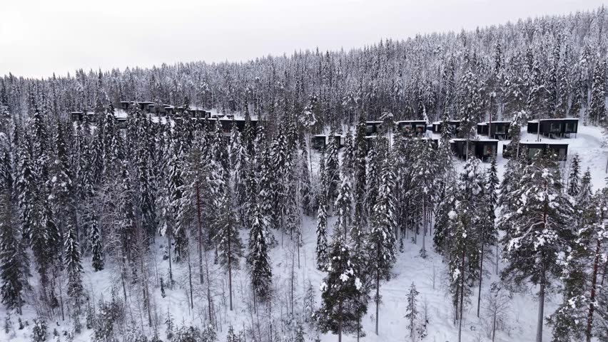Luxury winter hotel surrounded by pine forest covered in snow, Glass cabins, chalets near Santa Claus village, Lapland, Establishing drone shot