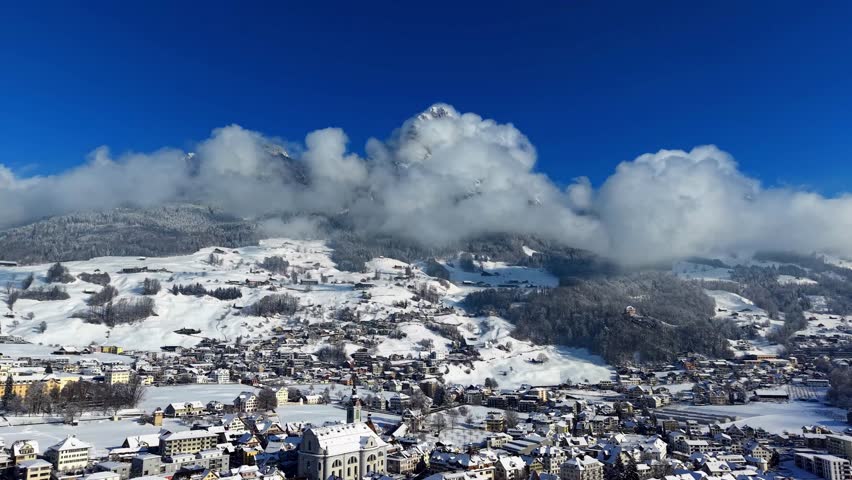 Cinematic drone footage of Schwyz village and St. Martin church, with the cloud-covered Grosser Mythen peak.