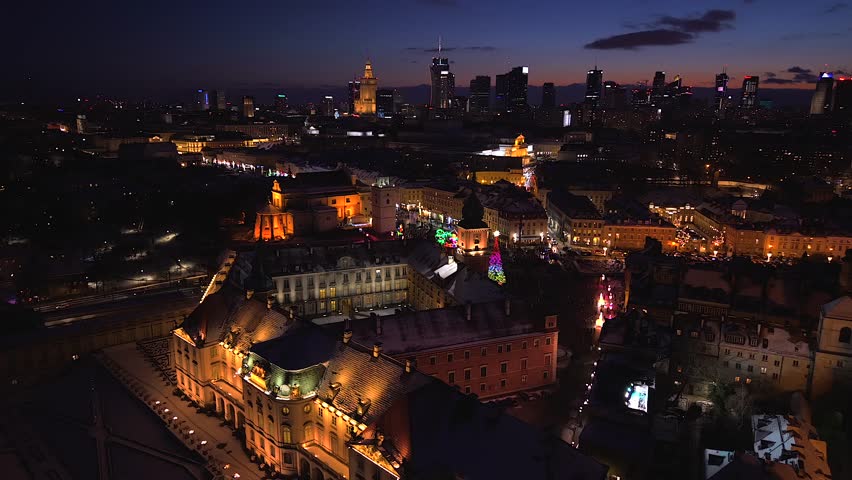Aerial night orbit over Warsaw Old Town with the Royal Castle, festive Christmas lights and glowing city skyline.
