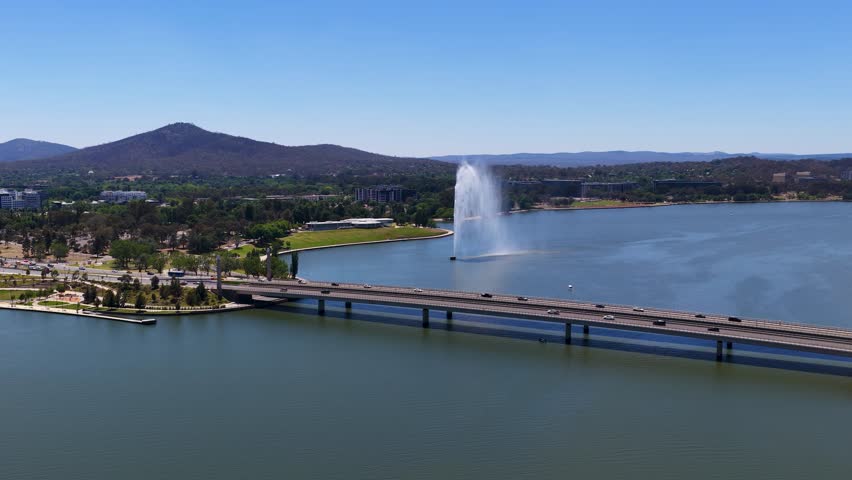 High angle drone shot of a large water fountain and bridge over a calm lake