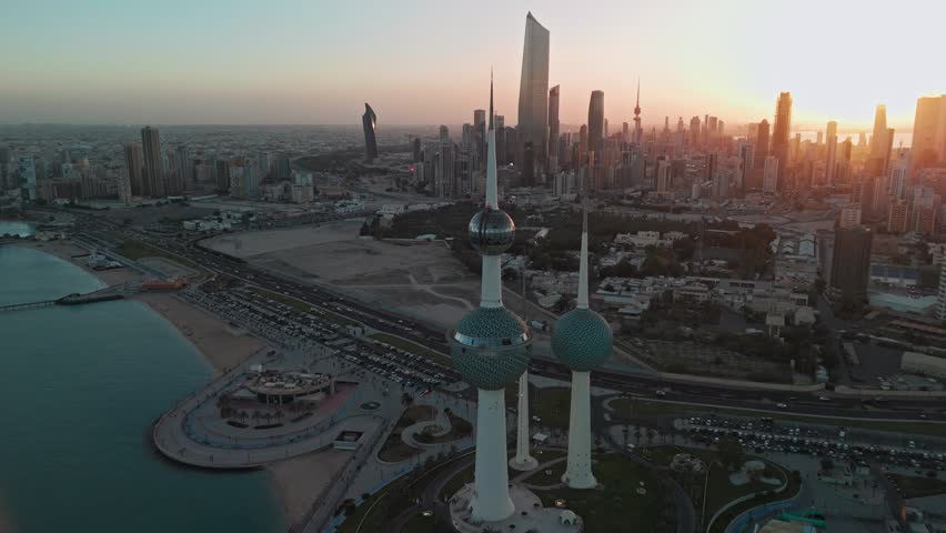 Cinematic drone aerial of Kuwait Towers at golden-hour sunset with Kuwait City skyline, Arabian Gulf coastline, waterfront park and promenade—perfect for travel, landmark, tourism visuals.
