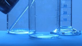 Clear liquid pouring into a graduated glass beaker in a science laboratory with blue light - Powered by Shutterstock - Get 15% off with code: PIKWIZARD15