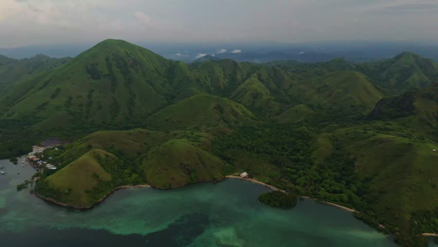 High altitude drone footage of the Flores landscape in Komodo National Park, Indonesia, captured during the rainy season, showing lush green hills, tropical coastline and calm turquoise bays in 4K.