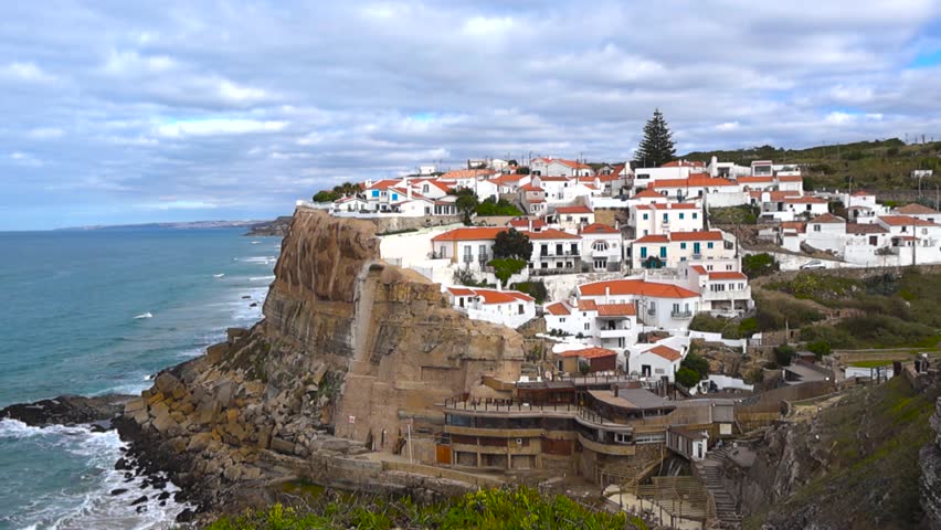 White houses with red rooftops cling to dramatic seaside cliffs, overlooking deep blue Atlantic water and creating a postcard like coastal village scene.