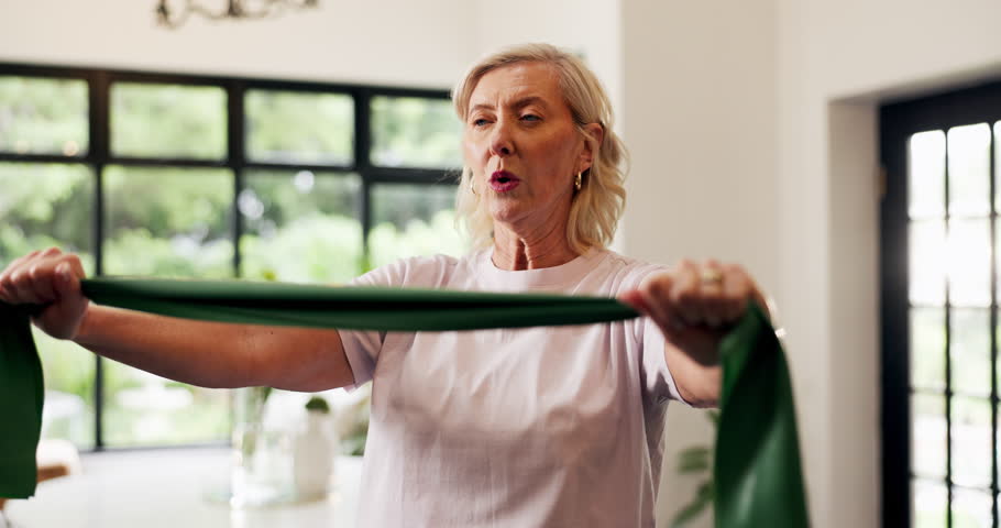 Breathing, fitness and resistance band with old woman in living room of home for rehabilitation. Equipment, exercise and stretching with senior person in apartment for strength training or workout