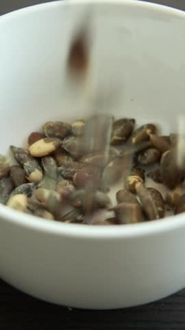 Close-up of pumpkin seeds falling into a small white bowl