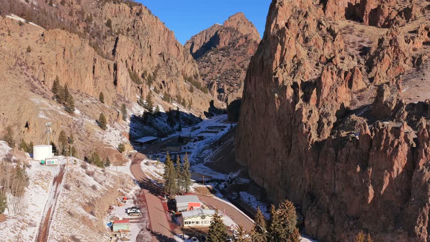 A cinematic aerial view captures the dramatic contrast between deep canyon shadows and a sunlit mountain peak. Steep rocky walls and rugged textures define the immense scale of this Southwest terrain.