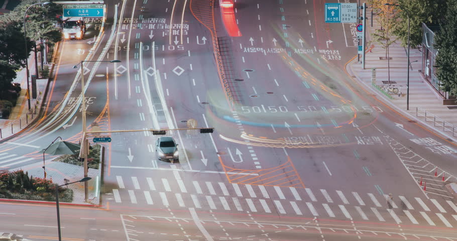 Time-lapse. Vehicles navigate a bustling intersection under night lights, capturing the continuous movement and energy of urban traffic with illuminated road markings and signals
