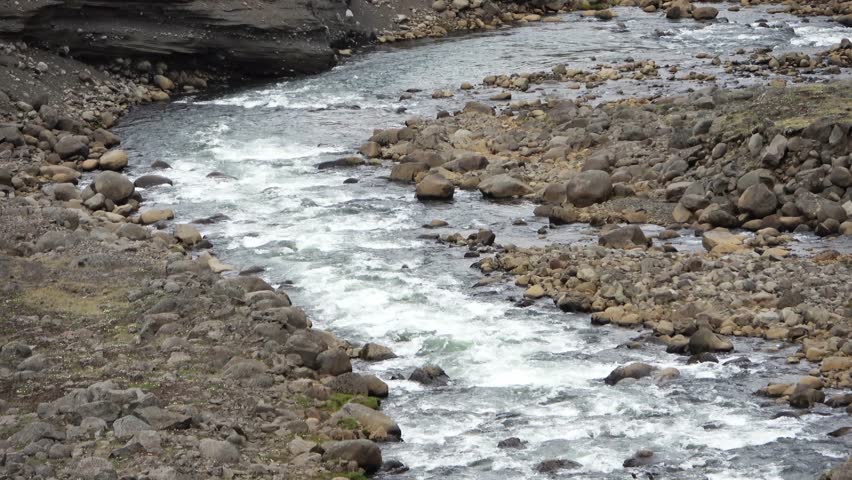 Mountain stream with clear water flowing rapidly over stones and boulders in a rugged valley
