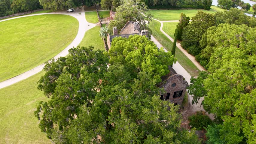 Drone footage over a historic plantation at Middleton Place in Charleston South Carolina showing lush green lawns massive oak trees and a small cottage among the trees.