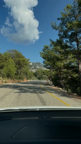Point of view from a car driving along a winding mountain road. Beautiful summer landscape with green pine trees and blue sky