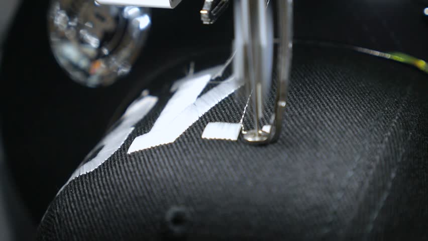 Industrial embroidery machine creating a white logo on a black baseball cap in an automated process, showcasing the precision and speed of modern textile manufacturing and customization