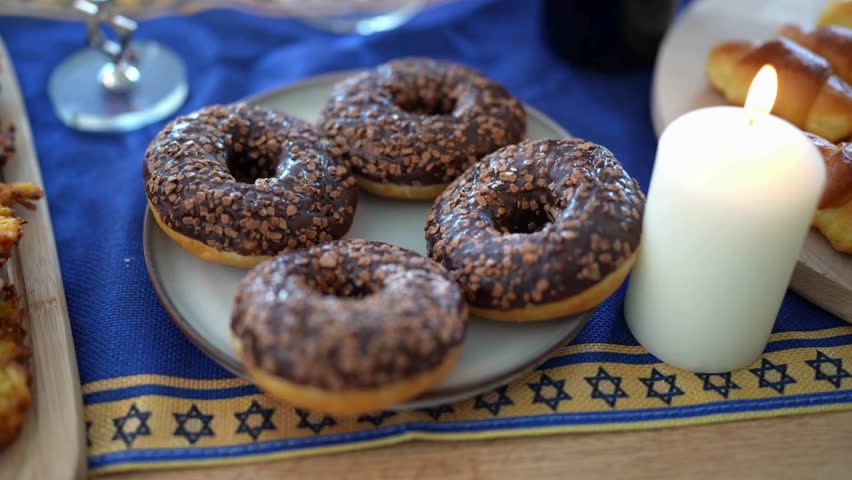 A plate of chocolate-glazed sufganiyah rests on a blue tablecloth decorated with the Star of David, showcasing a delicious Hanukkah pastry enjoyed during the Jewish holiday.