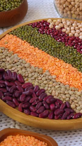 Various types of raw legumes, including beans, lentils, and chickpeas, displayed in colorful stripes on a rotating wooden plate, showcasing a rich source of vegan protein and fiber