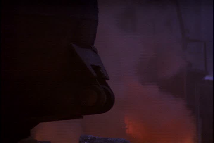 Steel works in Nizhny-Tagil, Russia. CU ladle with smoke and fire in background. Large hook drops from above and grabs ladle, pushing it out of frame. 