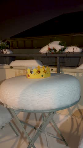 A golden paper crown rests on a snow covered outdoor table at night, symbolizing winter celebration and festive tradition.