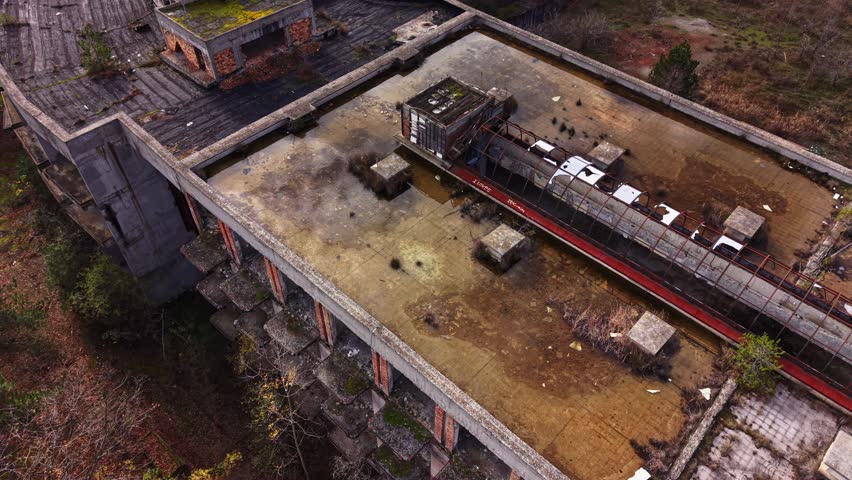 Aerial view captures an abandoned building rooftop with moss-covered surfaces, crumbling structures, and nature reclaiming the area, showcasing urban decay.