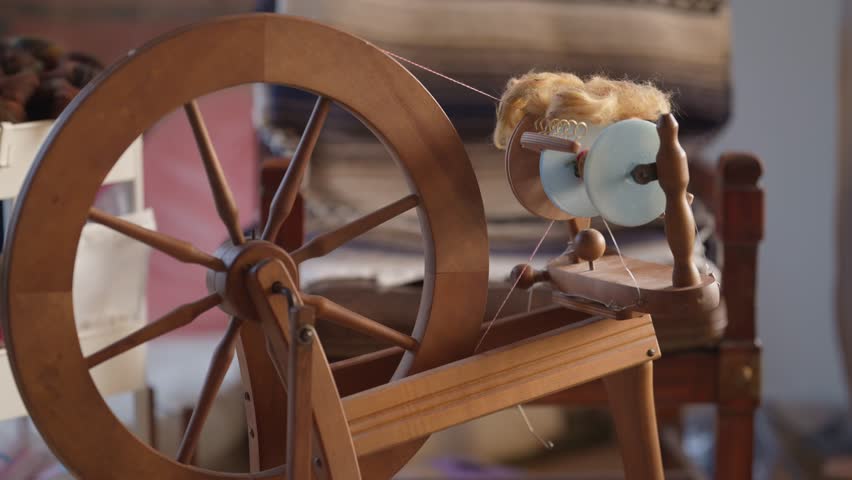 Home spinning wheel with 3d printed blue bobbin ready to use.  Wooden treadle spinning wheel with fiber and chair in the background.  Fiber arts and crafts at home with specialized tools.