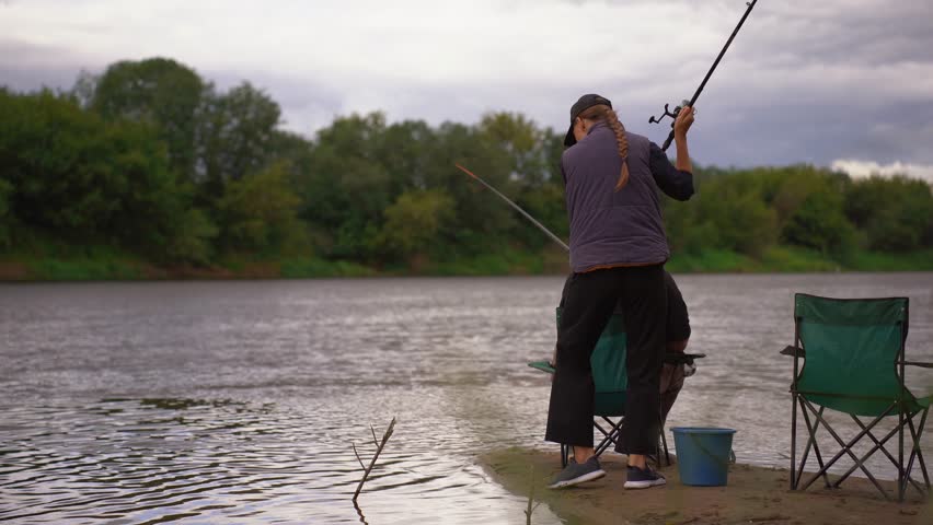 Young couple man and woman fishing on river bank on cloudy day. Spending time together. Relaxing family holidays by the river.