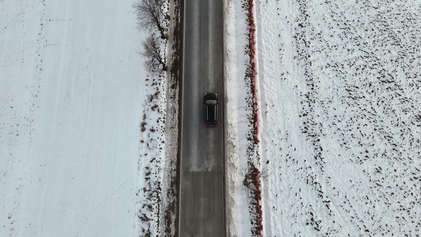 Aerial view of a car traveling along a snow-covered road surrounded by winter landscape showcasing continuous movement and progression through the snowy terrain and open fields. Follow to riding auto