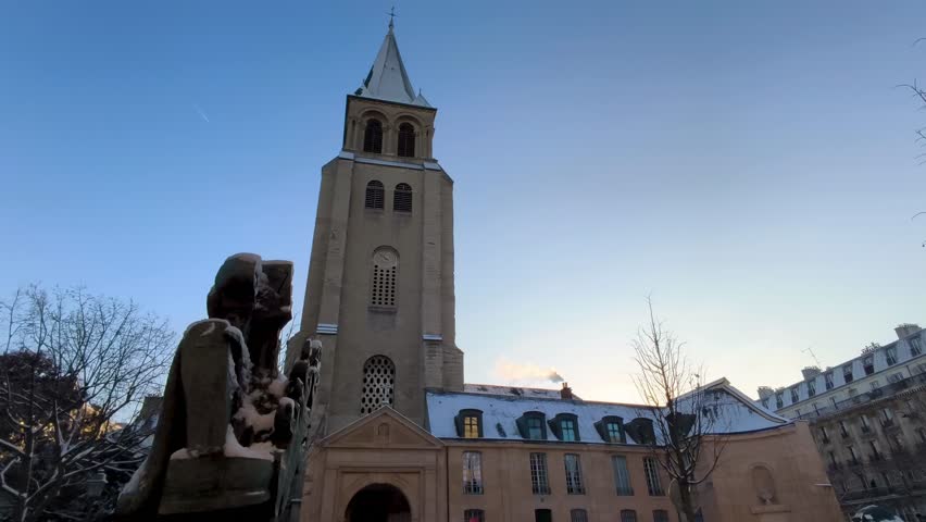A historic stone church tower rises above trees in Paris during winter under clear blue sky and cold light.