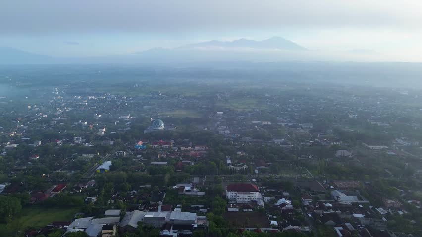 Misty aerial shot of a city with mountains on the horizon.