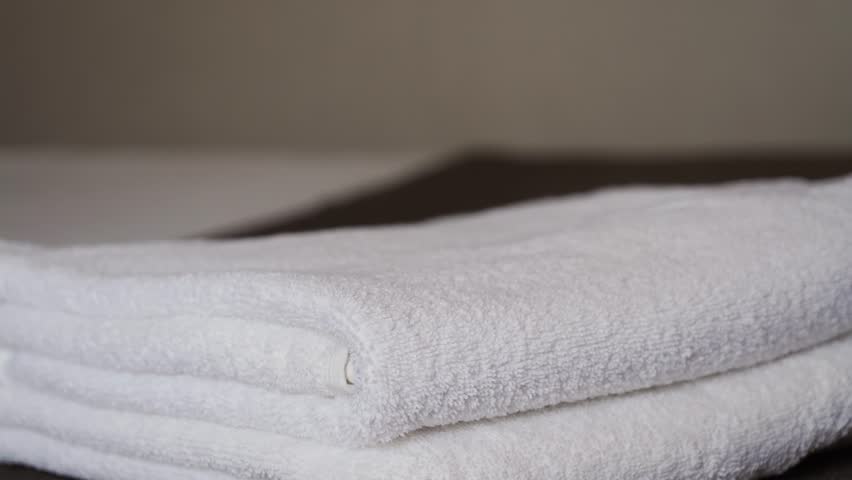 Close-up of hands placing white bath towels on the bed sheet. Concept of room cleaning service. High quality 4k footage