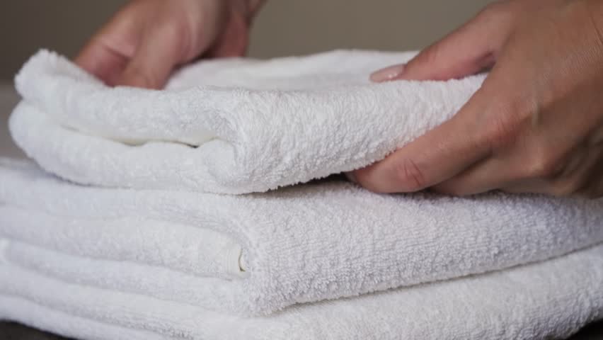 Close-up of hands placing white bath towels on the bed sheet. Concept of room cleaning service. High quality 4k footage