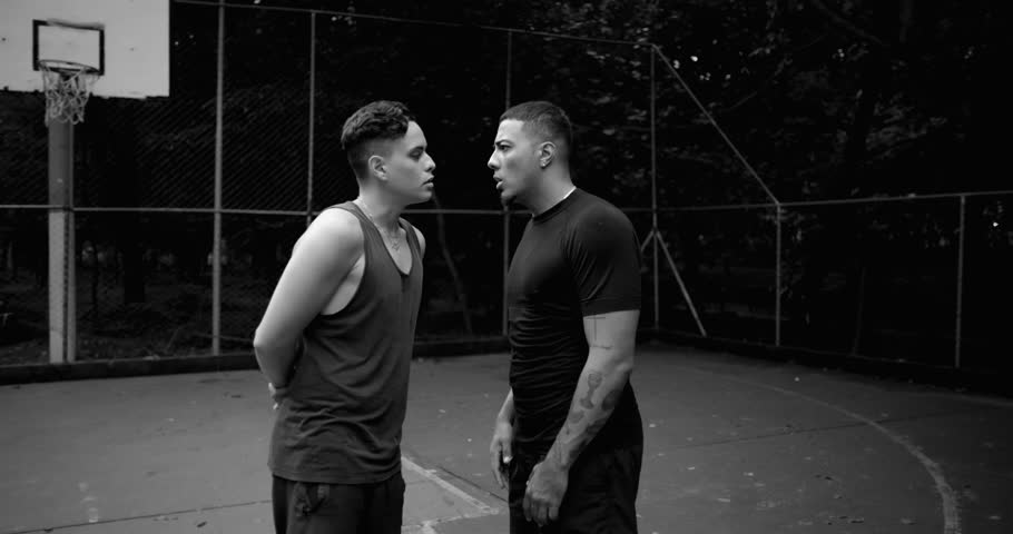 Two Hispanic men arguing face to face on basketball court, in black and white, finger pointing and intense expressions showing anger, pride, and confrontation