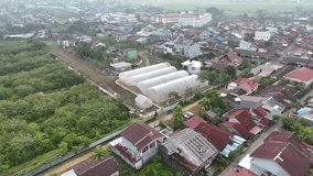 A view from an aerial drone of a foggy rural village on the outskirts of a city in Indonesia, showing large white circular greenhouses on open land. - Powered by Shutterstock - Get 15% off with code: PIKWIZARD15