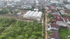 A view from an aerial drone of a foggy rural village on the outskirts of a city in Indonesia, showing large white circular greenhouses on open land. - Powered by Shutterstock - Get 15% off with code: PIKWIZARD15