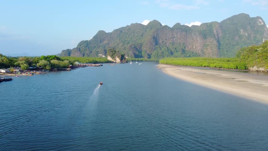 A serene coastal landscape with mountains, a river, and a boat traversing the waters in Krabi Province, Thailand. Amazing Thailand.