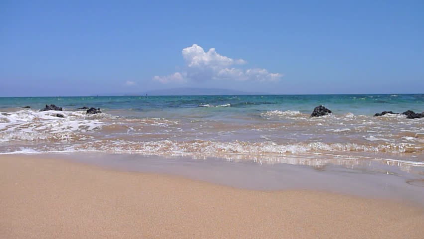 Waves crashing on sandy beach close in on camera and soak lens in sunny Hawaii.