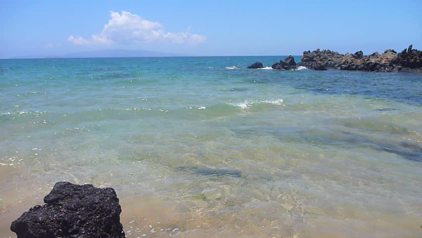 Waves gently crashing on sandy beach in sunny Hawaii.