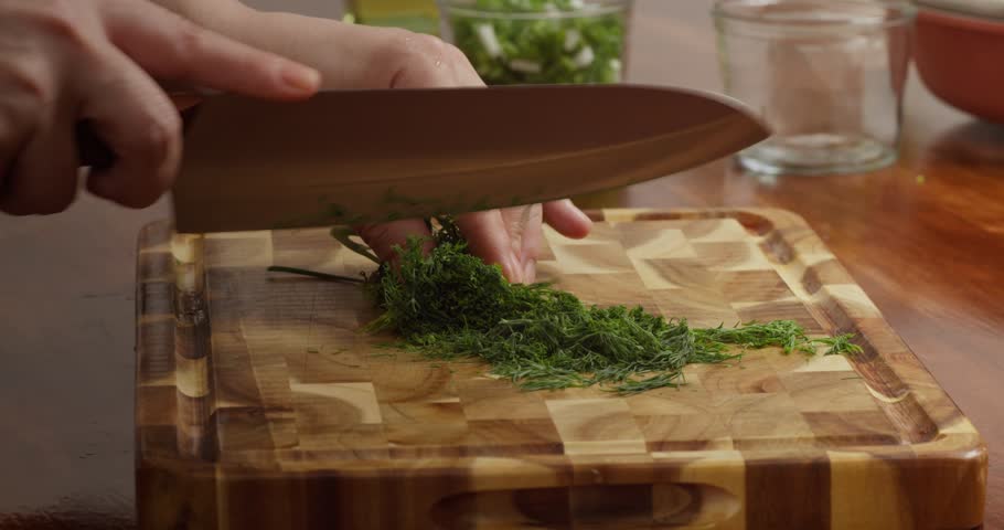 Of fresh herbs being chopped on a wooden cutting board over a wooden table. Shot of a chef chopping fresh spring onions, parsley, and dill on a wooden cutting board placed on a rustic