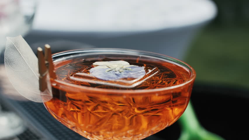 Orange cocktail with floral ice cube in crystal coupe glass
