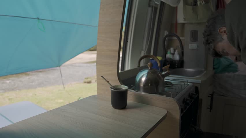 Interior view of a motorhome where a person is reaching for a mate cup next to a tray of freshly baked pizza with tomato slices
