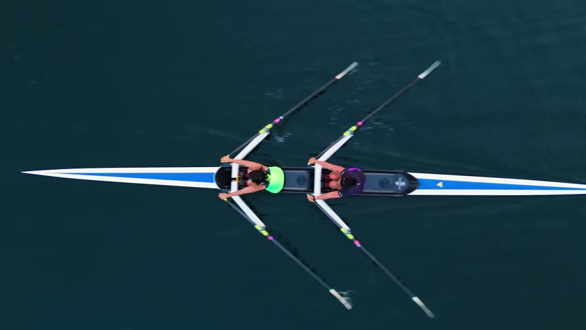 Top View Four young athletes row together in an eight-oar boat during sunrise training. Serene ocean and warm morning light frame focused preparation for rowing competition.