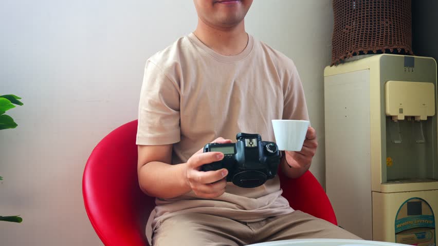 Young photographer sips coffee while reviewing photos on his DSLR camera during breakfast at home