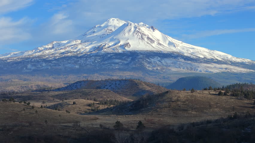 Snow covered Mount Shasta towers over rolling hills and open plains, showcasing a dramatic volcanic landscape in Northern California, withskies depth, scale, and wilderness beauty