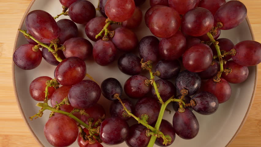 Fresh grapes fruits on a white plate rotation top view.
