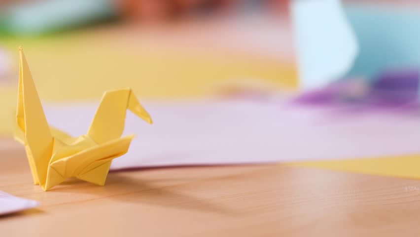 A close-up shot of a yellow paper crane on a desk with soft natural lighting