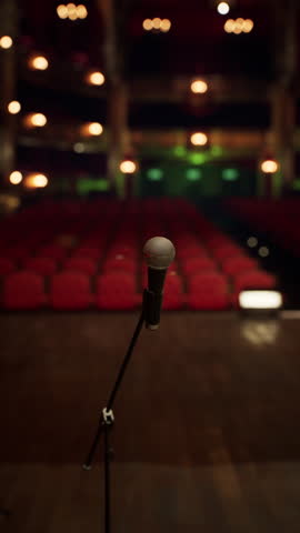 A single microphone stands on stage, awaiting the performer. The audience seats are empty, illuminated by warm lights, creating an atmosphere of anticipation in the opera house.