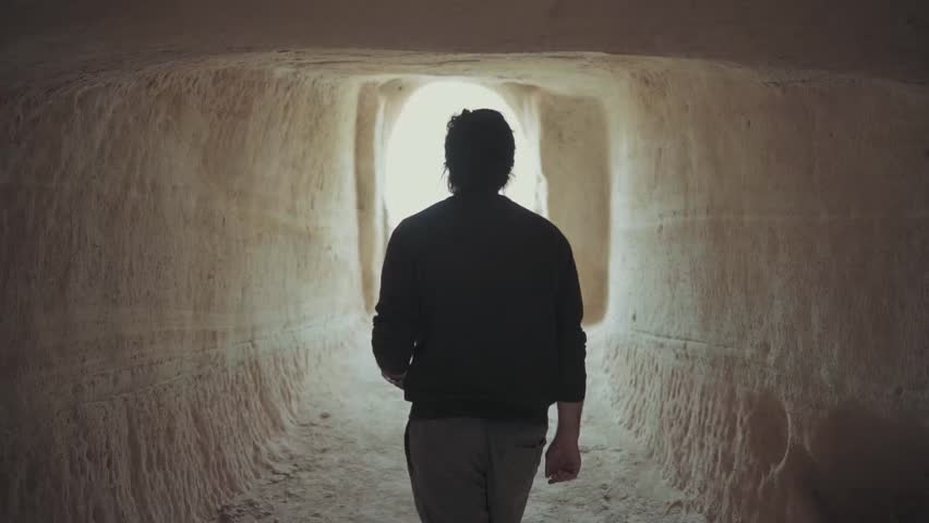 Silhouette of person walking inside tunnel toward light.