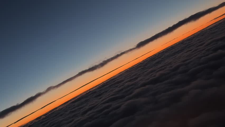Pilot’s view captured from cockpit of a golden horizon just before sunrise while doing a right turn over a layer of clouds.
