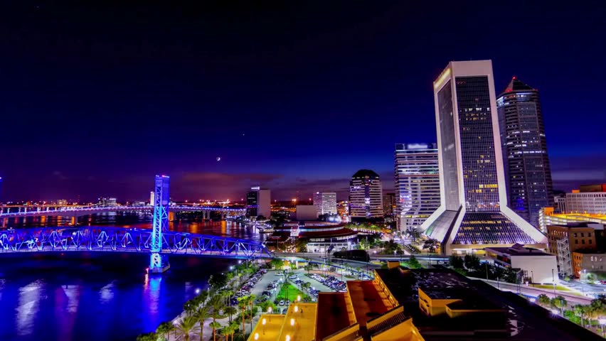 Night view of Jacksonville, Florida skyline with illuminated bridges, city lights reflecting on the water, highlighting urban beauty and nightlife.