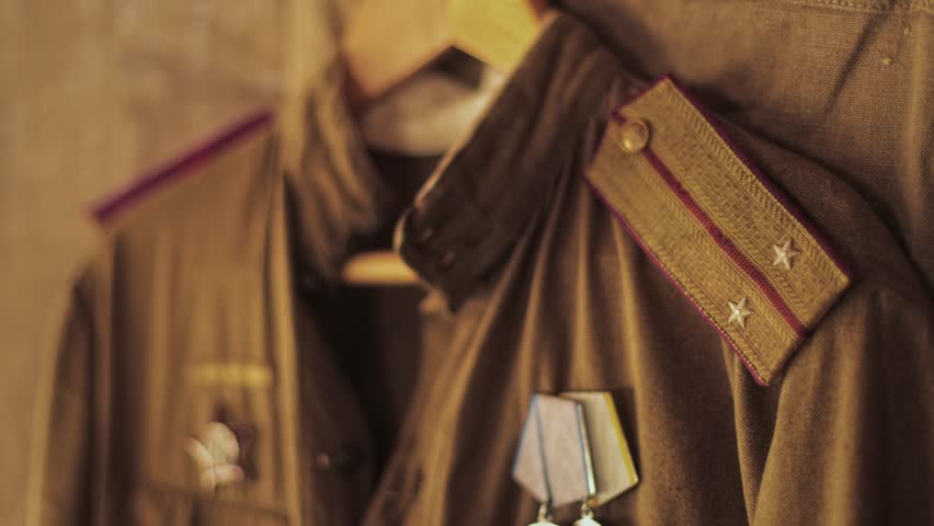 Close-up view of olive green Soviet officer uniform, prominent shoulder strap denoting rank of lieutenant, attached medals of honor below, historical war symbolism on display. Reenactment props