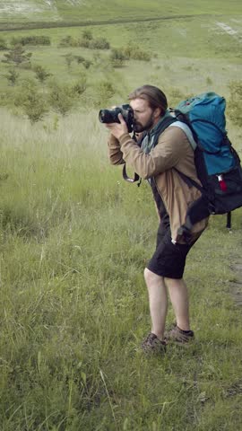 A man photographerstands on a hill taking photos with a camera while enjoying nature.