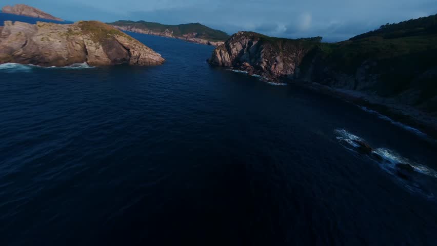 FPV flight along coastal cliffs, skimming above the ocean as waves crash below, capturing dramatic rock formations, speed, and a powerful cinematic seascape at golden hour.