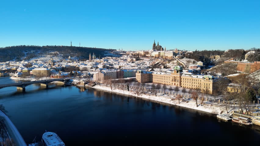 Aerial view of snowy Prague, Czech Republic. Winter cityscape with Snow-covered rooftops, Vltava River, and sunny blue sky